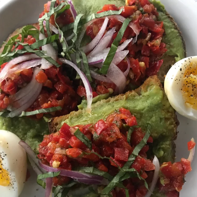 Avocado toast topped with chopped cherry tomatoes, red onion and greens
