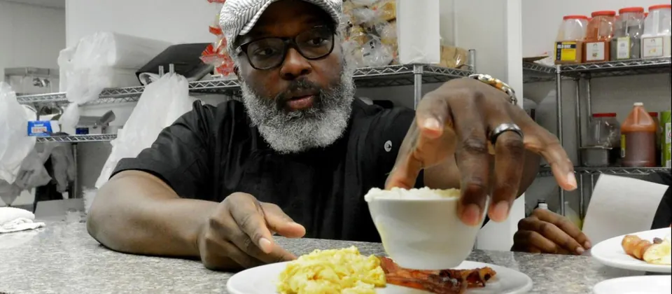 Chef Clifford Rome in a cap and glasses spooning food onto a plate