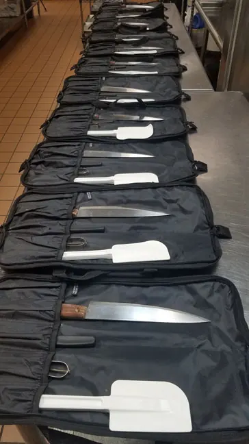 A row of open knife kits laid out on a long table
