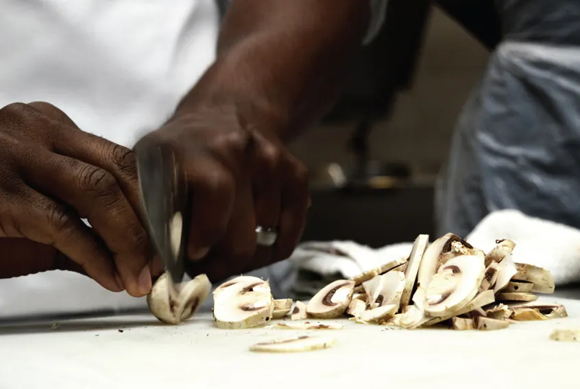 Close-up of a cook slicing mushrooms on a white cutting board
