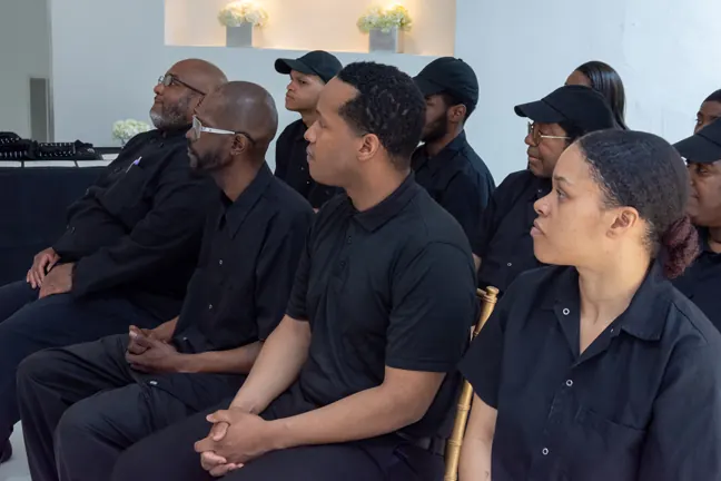 Students in black polos and caps seated attentively at a ceremony