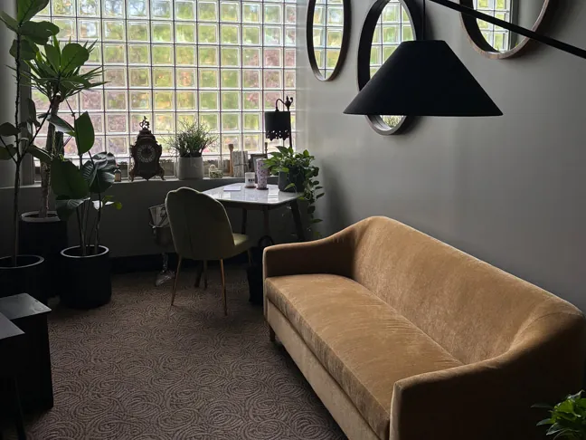 The Sound Lounge: a tan velvet sofa, a workstation and a glass-block window with plants